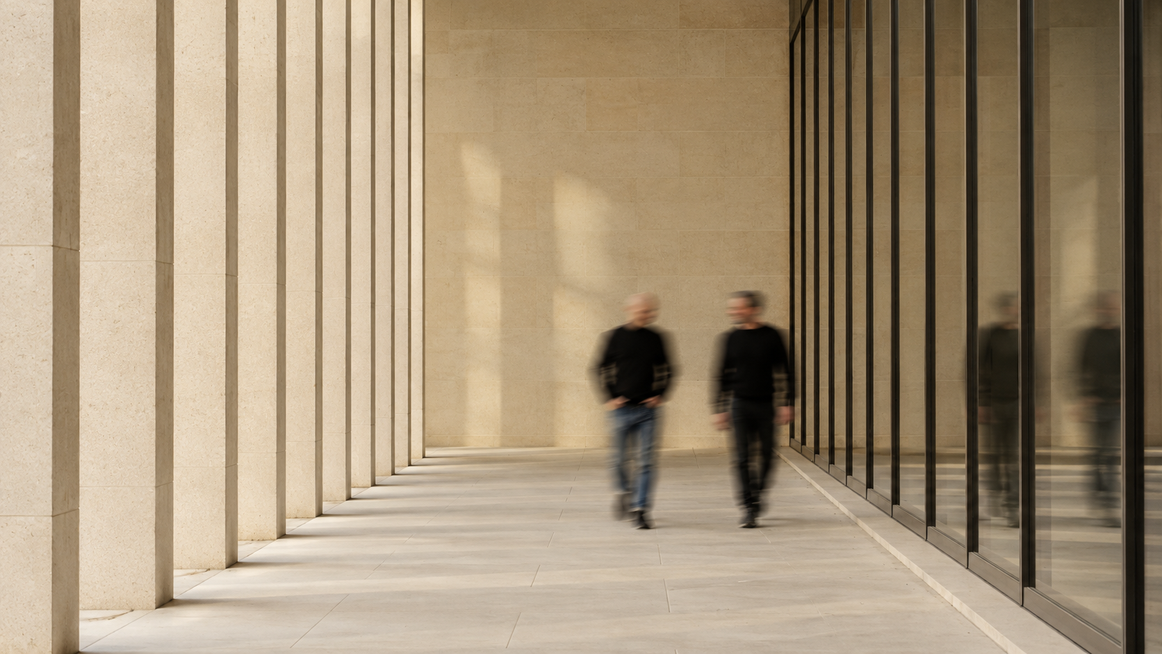 Two professionals walking in motion through a sunlit stone colonnade
